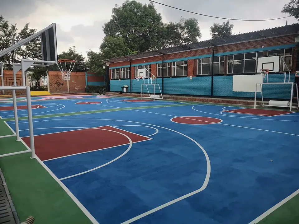 Cancha multideportiva de colegio recién pintada con estructuras de baloncesto