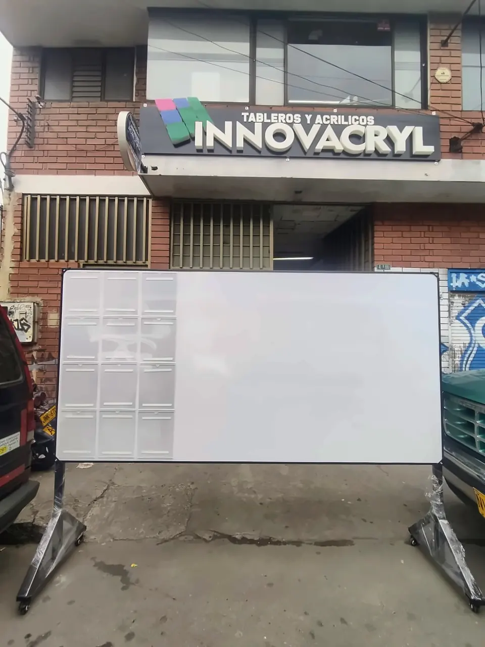 Tablero de escritura blanco sobre estructura rodante, frente a un local comercial